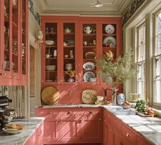 a kitchen with red cabinets and marble counter tops, along with an open window to the outside