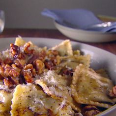 a white bowl filled with pasta covered in cheese and nuts on top of a wooden table