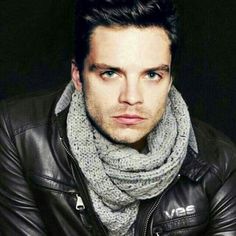 a man wearing a black leather jacket and gray scarf is looking at the camera with an intense look on his face