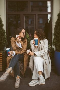 two women are sitting on the steps drinking coffee and talking to each other while holding cups