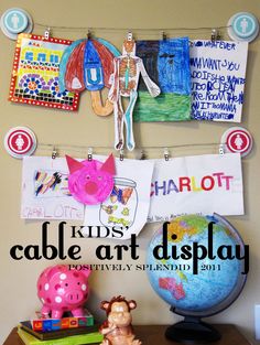 an art display with children's artwork hanging on the wall and toys sitting on top of it