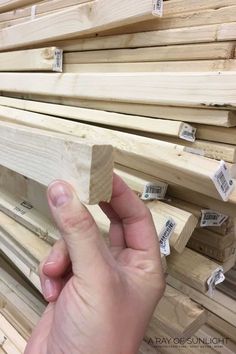 a hand is holding some wood in front of stacks of wooden planks with price tags on them