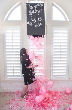 a woman standing in front of a window surrounded by pink balloons and confetti