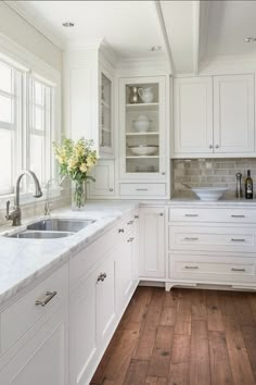 a kitchen with white cabinets and wood floors is pictured in this image, there are flowers on the window sill