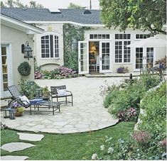 an outdoor patio with chairs and tables next to a large white house in the background