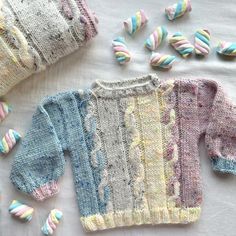 three knitted sweaters and two hats on a white table with colorful yarn sprinkles