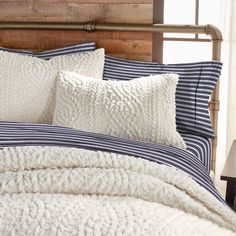 a bed with white and blue pillows on top of it next to a wooden headboard