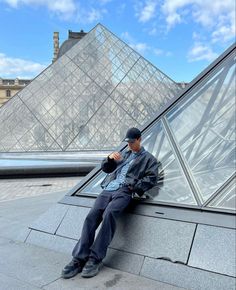 a man sitting on top of a roof next to a pyramid shaped glass building in the background