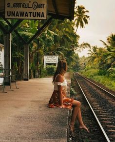 a woman sitting on the side of a train track next to a sign that says unawatuna