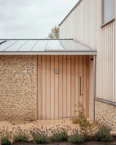 a brick building with a metal roof next to some plants and flowers in front of it