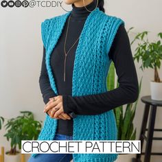 a woman wearing a blue crochet vest and black turtle neck sweater in front of a potted plant