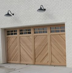 two lights on the side of a white brick building and a brown wooden garage door