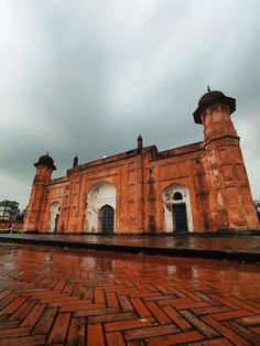 an old brick building with two towers on the top and one at the bottom, in front of a cloudy sky