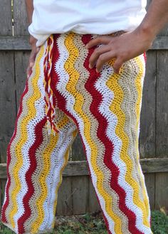 a person standing in front of a wooden fence wearing yellow and red crocheted pants