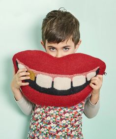 a young boy holding up a knitted pillow with a smile on it