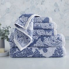 blue towels stacked on top of each other in front of a vase and wallpaper