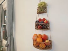 three baskets filled with fruit hanging from the side of a wall next to a window