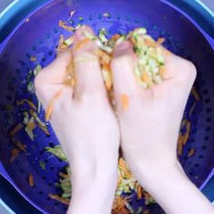 two hands in a blue colander with shredded carrots and other food scraps