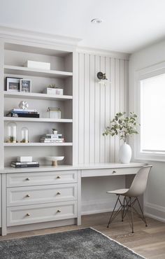 a white desk sitting in front of a window next to a chair and bookshelf