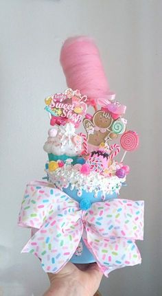 a person holding up a pink and blue cupcake with lots of candy on it