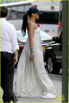 a woman walking down the street in a white dress and black hat with her hand on her hip