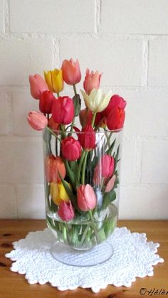 a glass vase filled with colorful tulips on top of a doily next to a brick wall