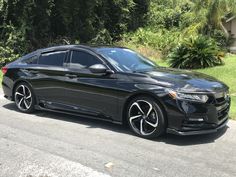 a black car is parked on the side of the road in front of some trees