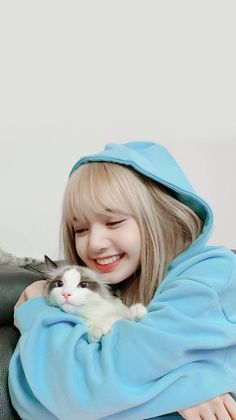 a girl in a blue robe holding a white and gray cat on her lap while smiling at the camera