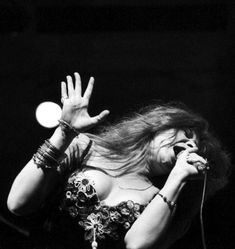 a woman with long hair holding her hands up in the air as she sings into a microphone