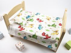 a toy bed with toys surrounding it on a white tablecloth and wooden blocks in the foreground