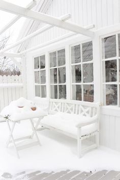 a white bench sitting in front of a window covered in snow next to a table