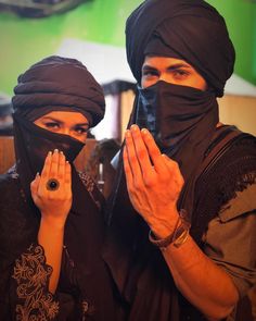 two people with black headscarves covering their faces, one holding her hands up to her face