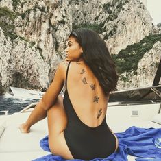 a woman sitting on the back of a boat in a black swimsuit with tattoos