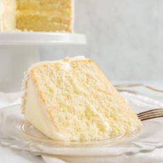 a slice of white cake on a plate with a fork next to it and the rest of the cake in the background