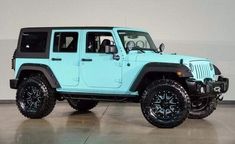 a light blue jeep is parked in a large room with black wheels and rims