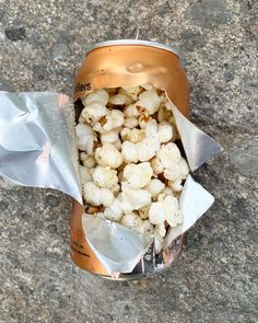 a can filled with popcorn sitting on top of a cement floor next to a silver bag