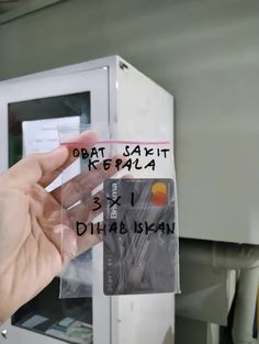 a person holding up a plastic credit card in front of a machine with words on it