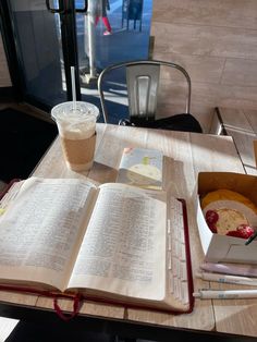 an open book sitting on top of a wooden table next to a cup of coffee