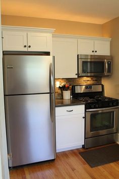 a stainless steel refrigerator and stove in a kitchen with white cabinets, wood flooring and hardwood floors