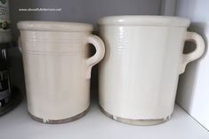 two white cups sitting next to each other on top of a shelf in a kitchen