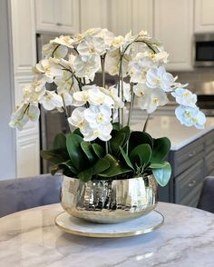 white flowers are in a silver vase on a marble table