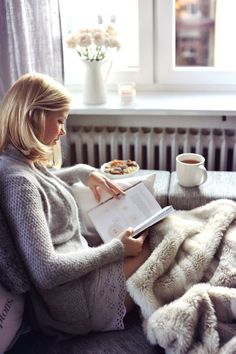 a woman sitting on a couch reading a book and holding a coffee cup in her hand