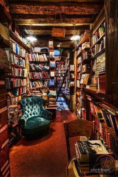 a room filled with lots of books next to a green chair and table in front of a book shelf