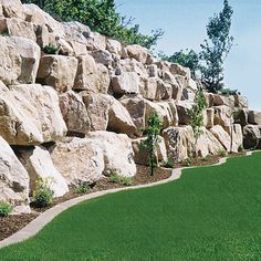 a large rock wall next to a lush green field