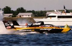 a speed boat speeds across the water near a large white boat in the background, with another boat behind it