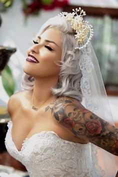 a woman with grey hair wearing a white veil and tattoos on her arm is smiling at the camera