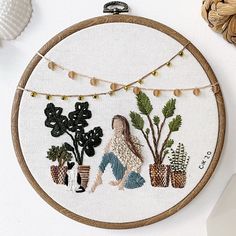 a woman is sitting in front of some potted plants on a white wall hanging from a wooden hoop