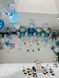 a table topped with lots of blue and white balloons, cupcakes and cake