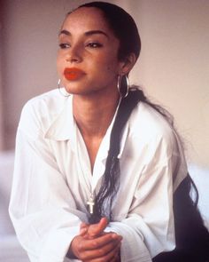 a woman sitting on the ground with her hands crossed and wearing earrings, looking off to the side