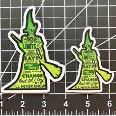 two green stickers with words on them sitting next to a ruler and measuring tape